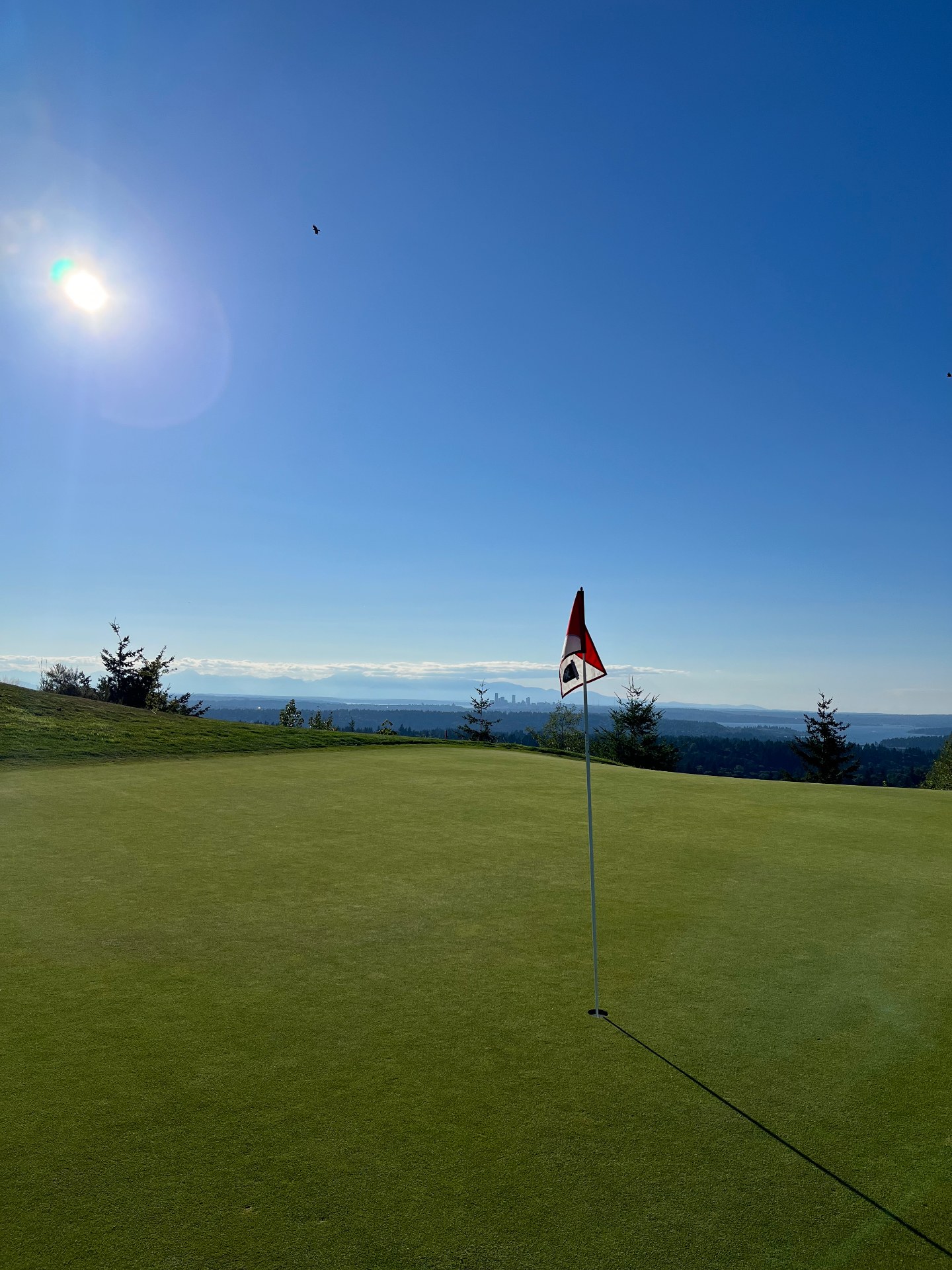 Hilltop green with red flagstick at Newcastle Golf Club Coal Creek Course, overlooking Lake Washington, Puget Sound and the distant Seattle skyline