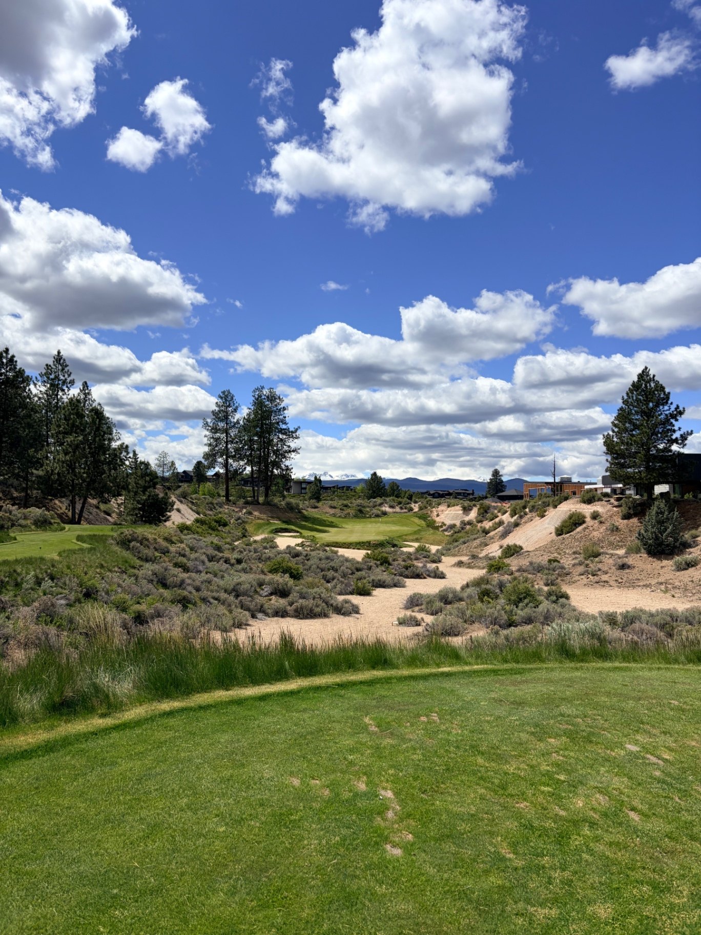 Tee view at Tetherow Golf Club over high-desert sand and sage to a green with the Cascade peaks beyond
