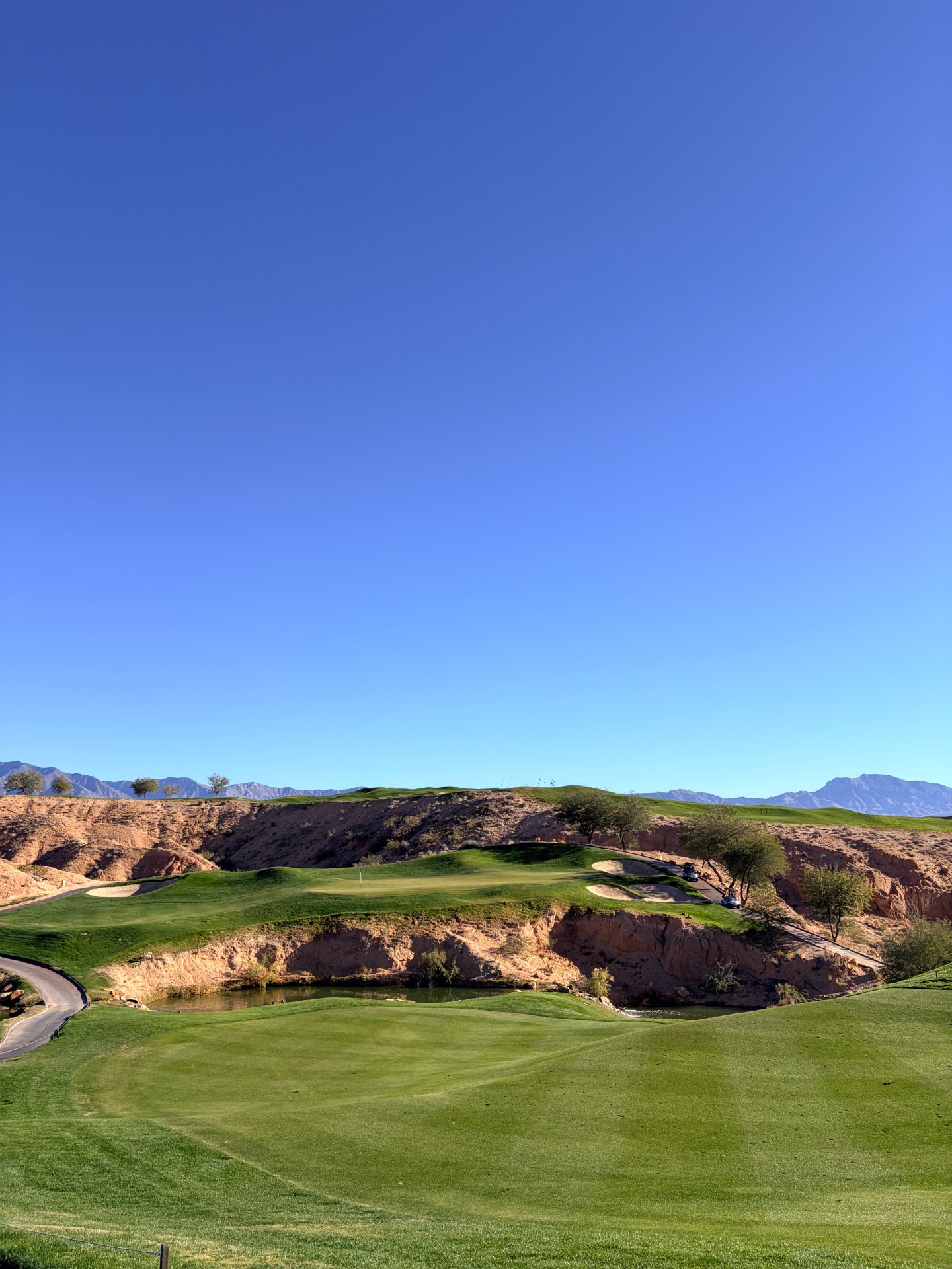 Desert golf hole at Wolf Creek in Mesquite, Nevada with green fairway, red rock canyon, pond and distant mountains