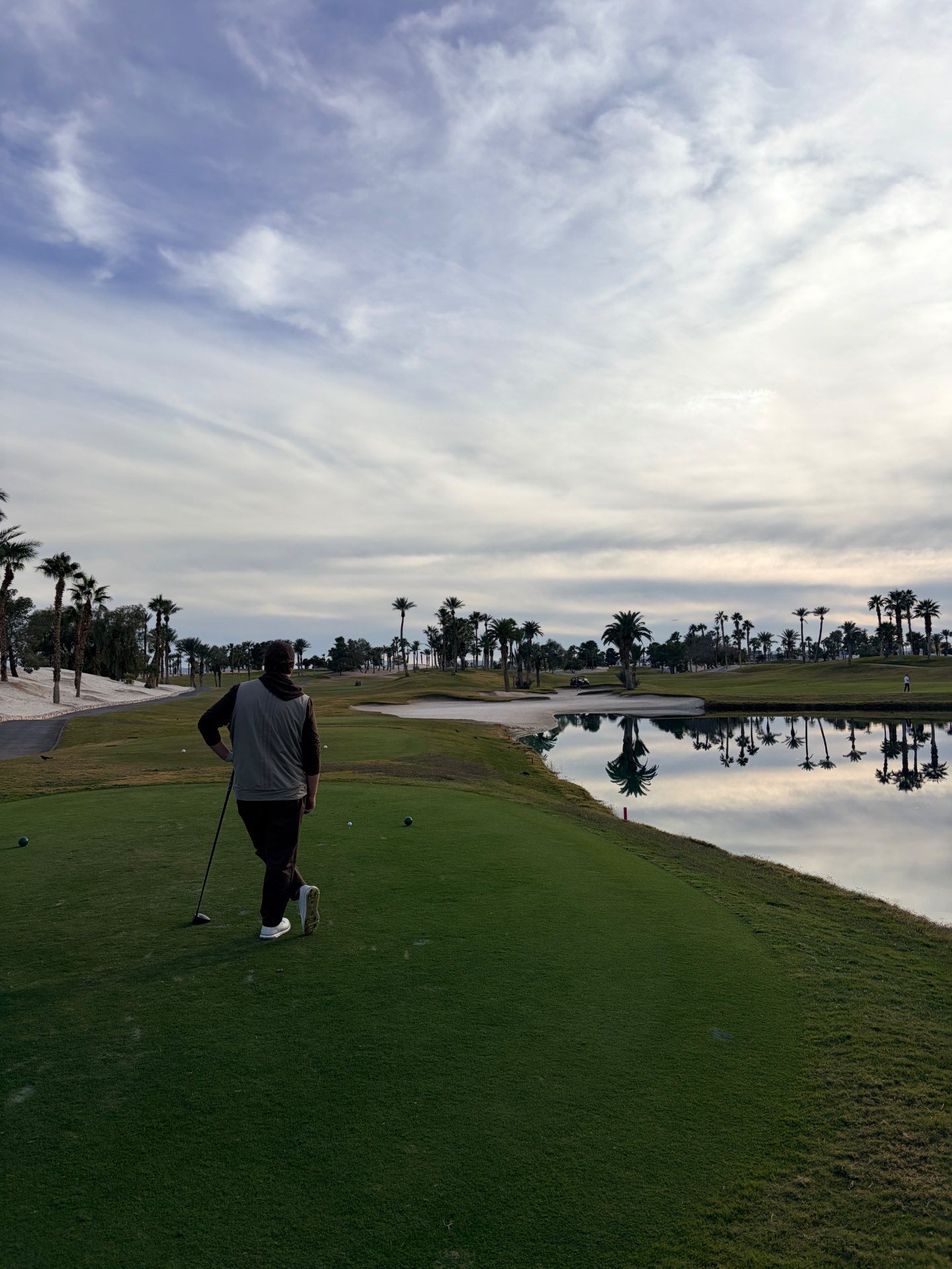 Golfer on the tee at Bali Hai Golf Club with palm trees reflected in a lake at dusk