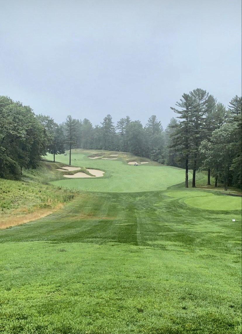 Misty morning view up a wide fairway at Red Tail Golf Club in Devens, Massachusetts, with staggered sand bunkers and tall pines framing an uphill green