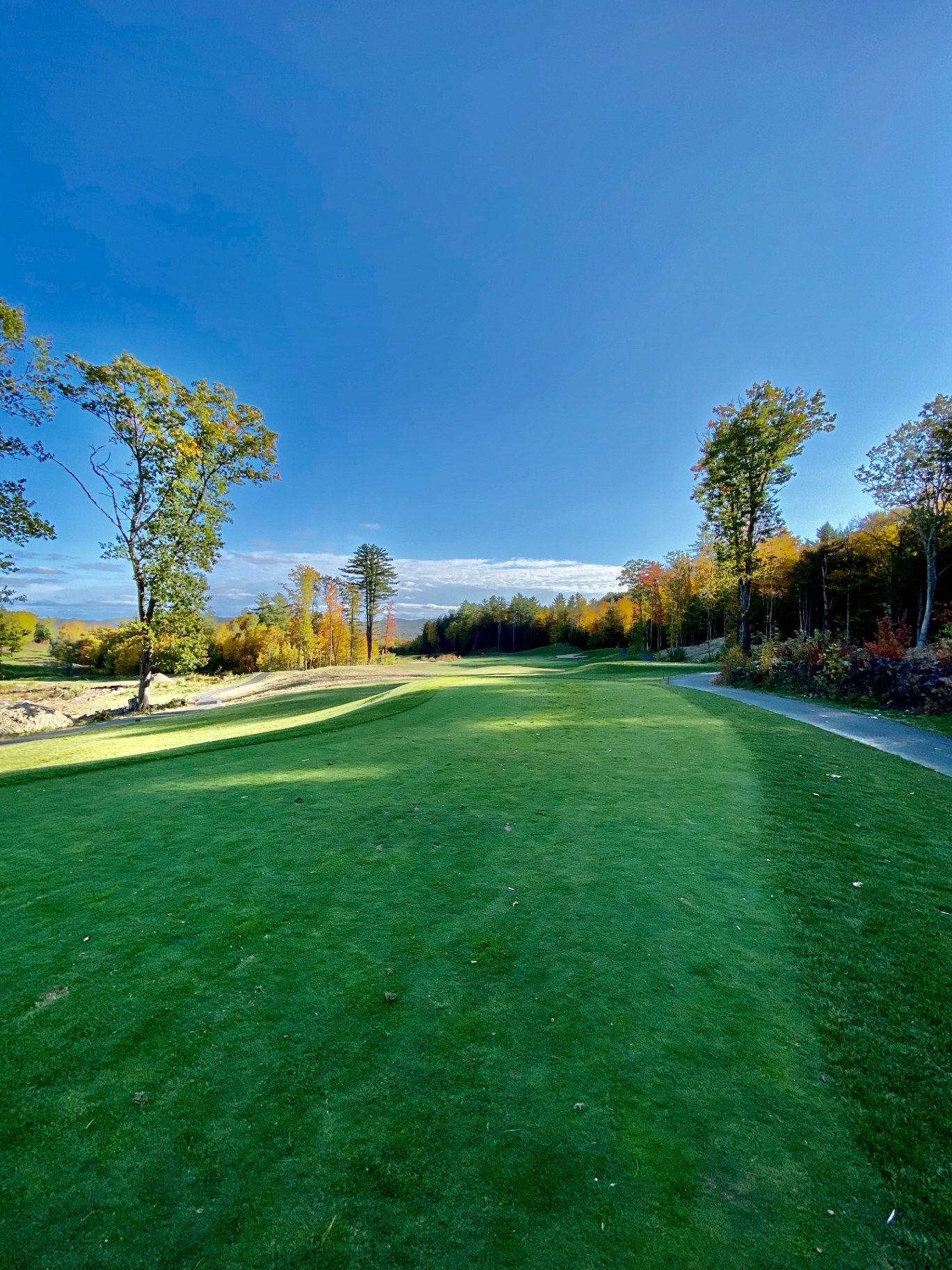 Tee view down a tree-lined fairway at Lochmere Golf & Country Club in Tilton, New Hampshire, with peak autumn foliage and a deep blue sky