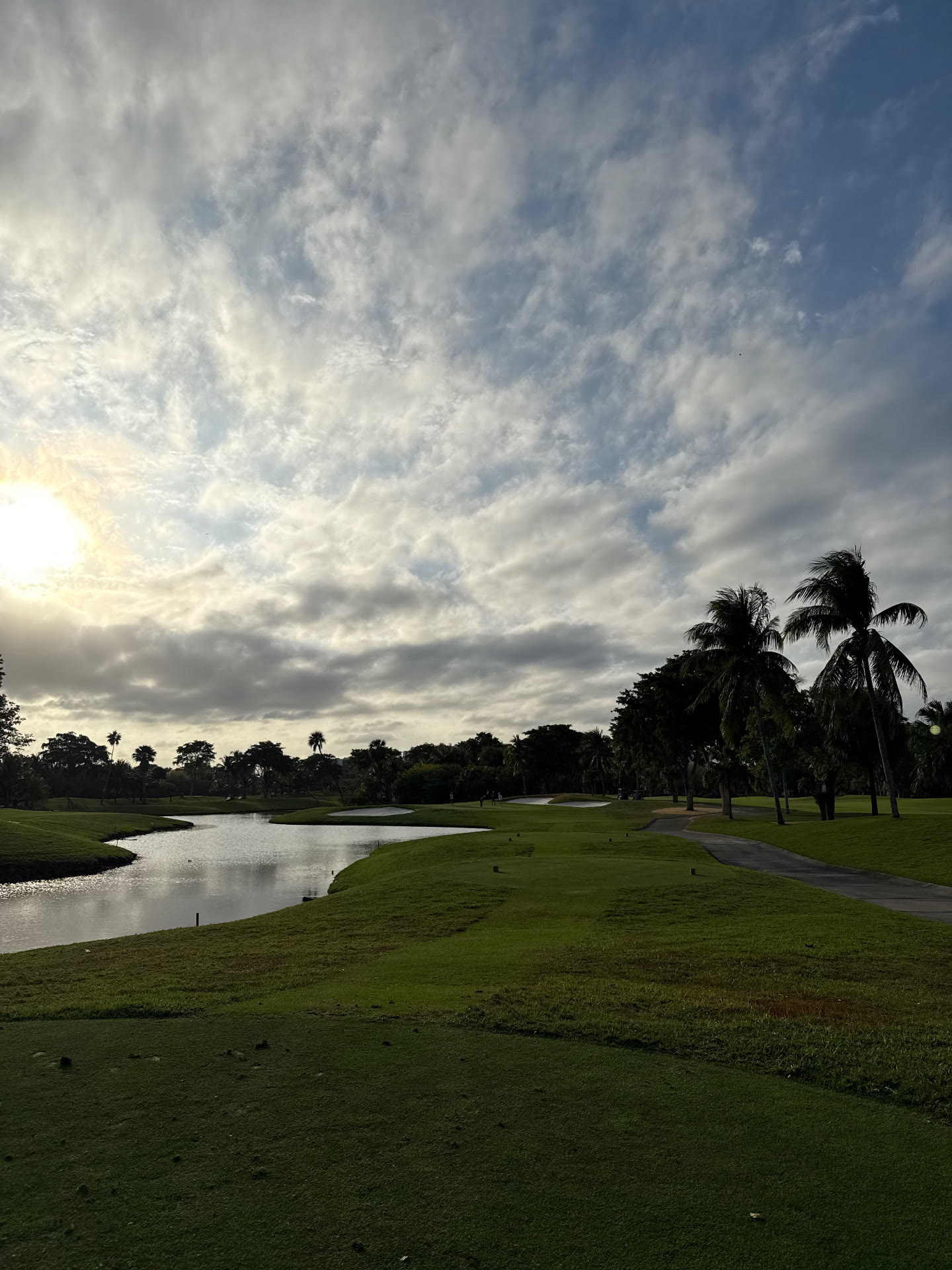 Early morning view across a winding lake toward bunkered greens and coconut palms on the Miller Course at Turnberry Isle Resort in Aventura, Florida