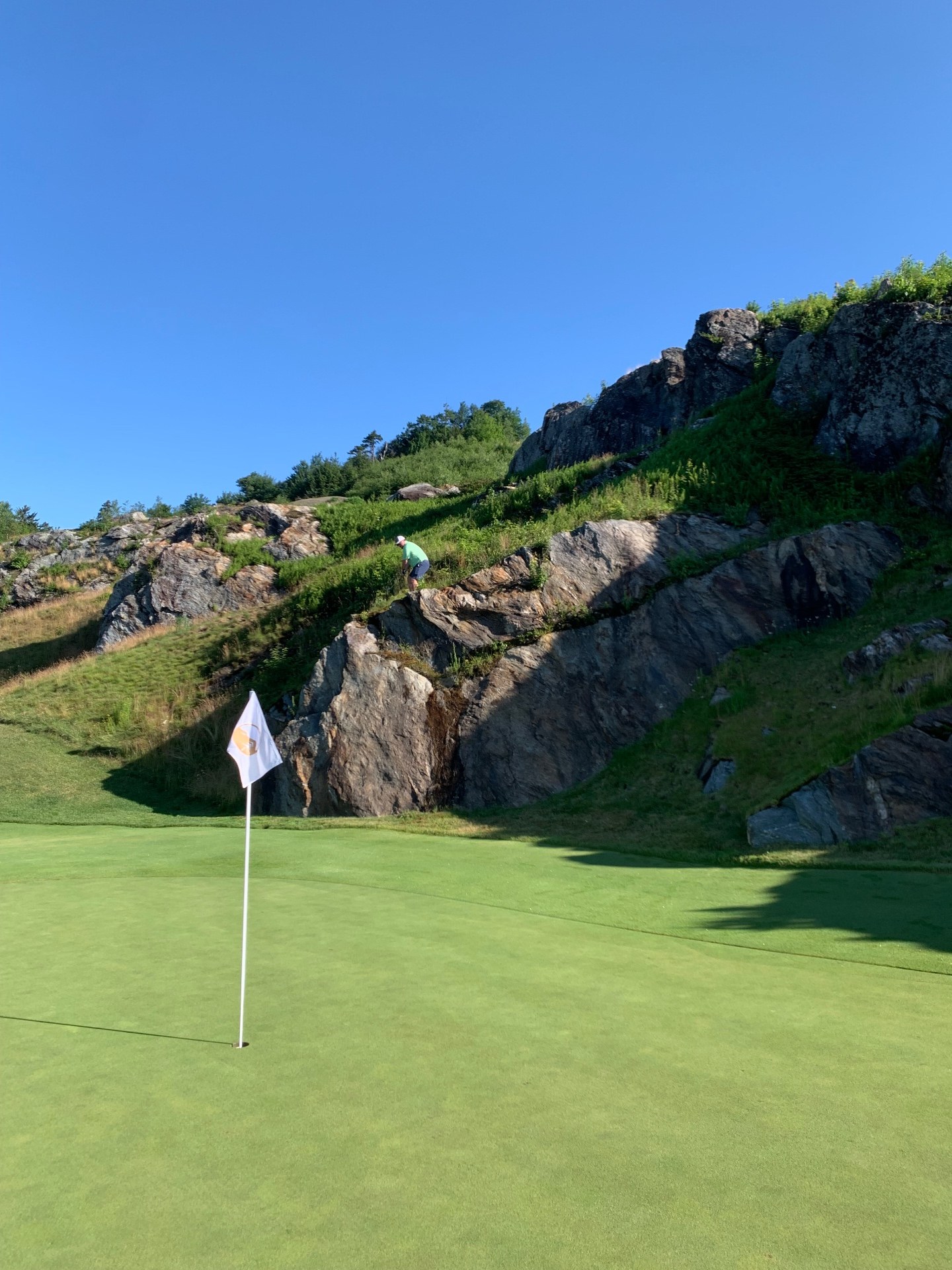 Green at Spruce Peak - The Mountain Course in Stowe, Vermont, tucked beneath a steep granite ledge with a golfer walking the hillside above