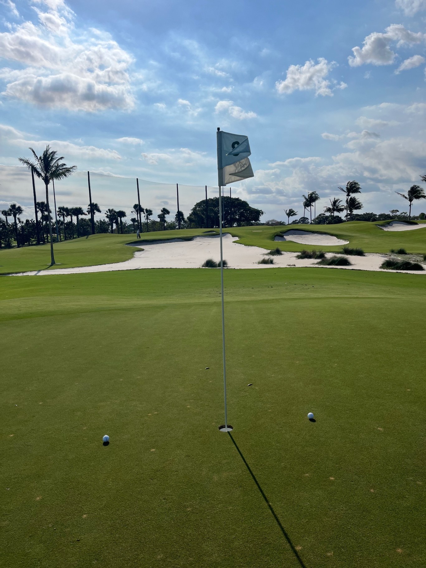 Green and flagstick at The Lit 9 at The Park West Palm in West Palm Beach, Florida, with white sand bunkers and palm trees under a blue sky