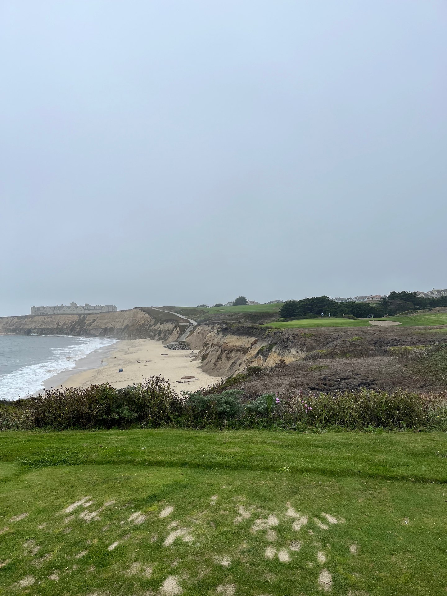 Clifftop green above the Pacific beach and bluffs at Half Moon Bay Golf Links Ocean Course on a foggy day