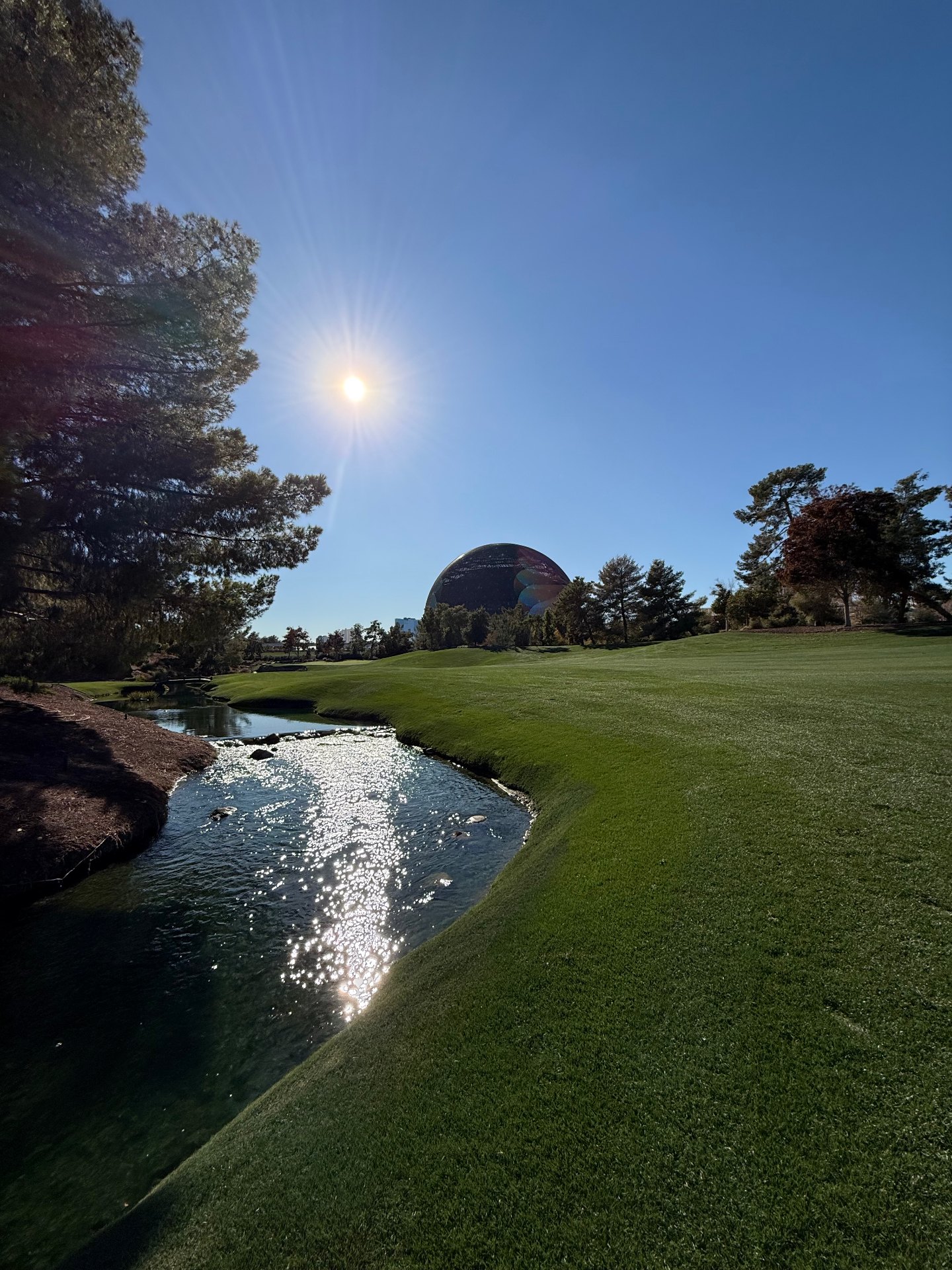 Creek winding along a manicured fairway at Wynn Golf Club with the Las Vegas Sphere in the distance