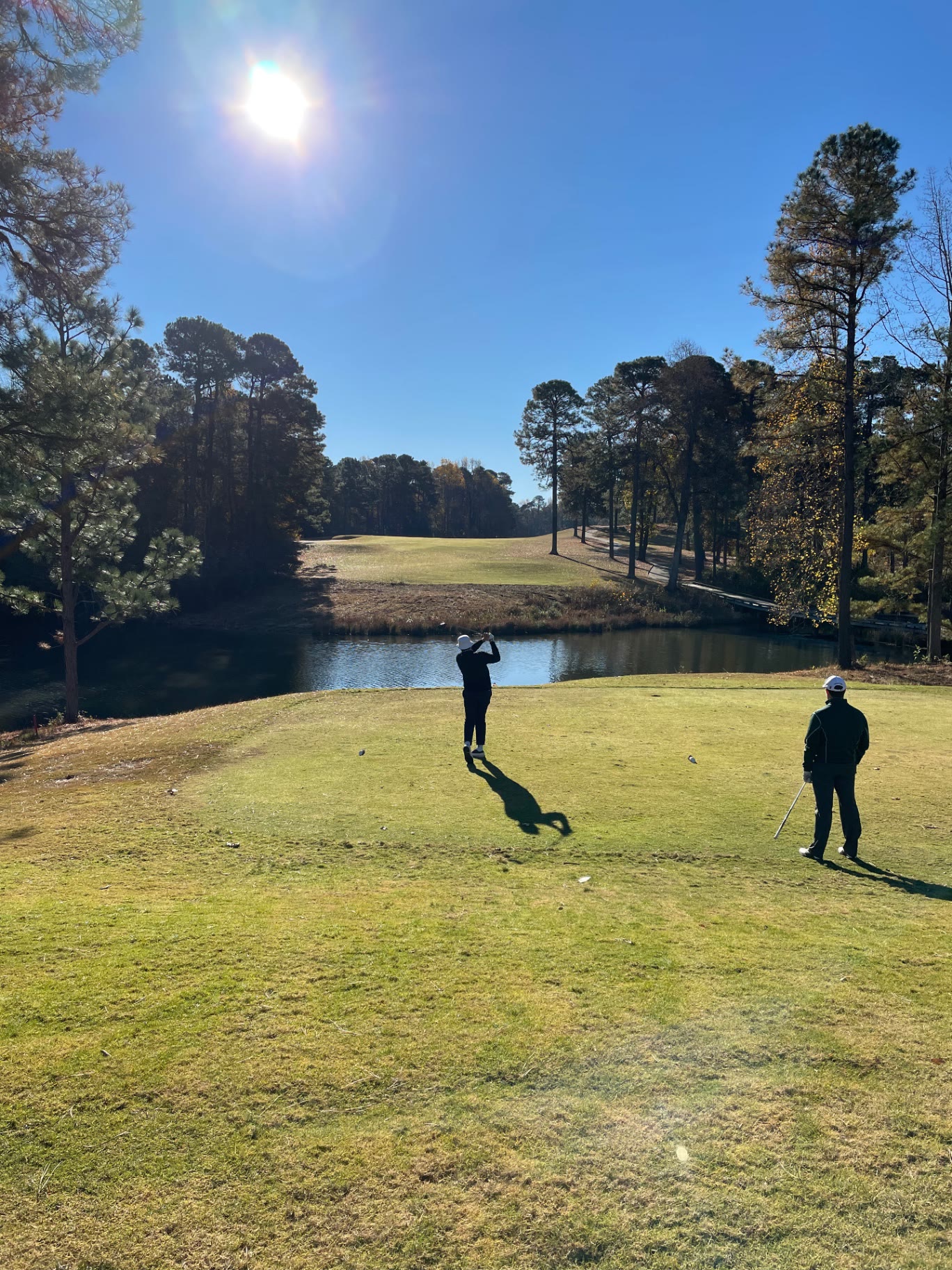 Golfer teeing off across a pond toward a pine-framed fairway at Pinehurst No. 8 in Pinehurst, North Carolina