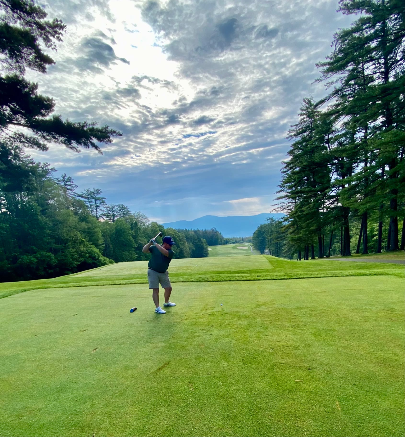 Golfer teeing off down a pine-lined fairway toward Adirondack mountains at Sagamore Golf Course in Bolton Landing, New York