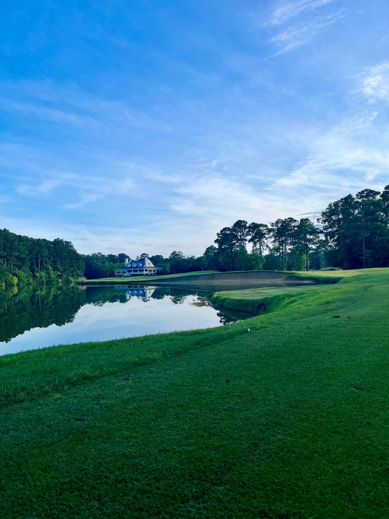Calm lake reflecting the clubhouse and pines at True Blue Plantation in Pawleys Island, South Carolina, with a large sandy waste bunker beside the green