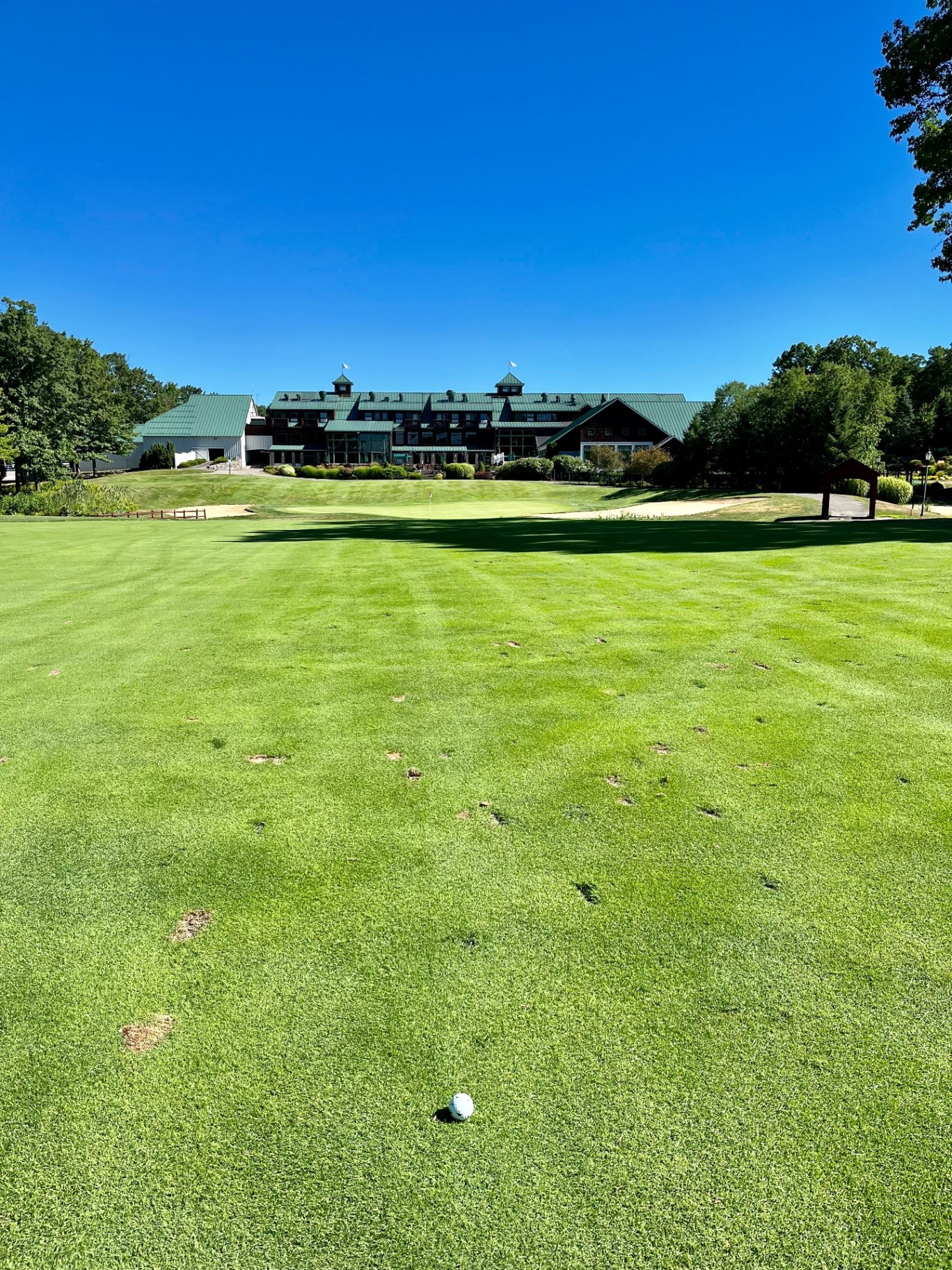 Ball on a striped fairway looking uphill to a green fronted by bunkers with the green-roofed clubhouse behind at Atkinson Resort & Country Club