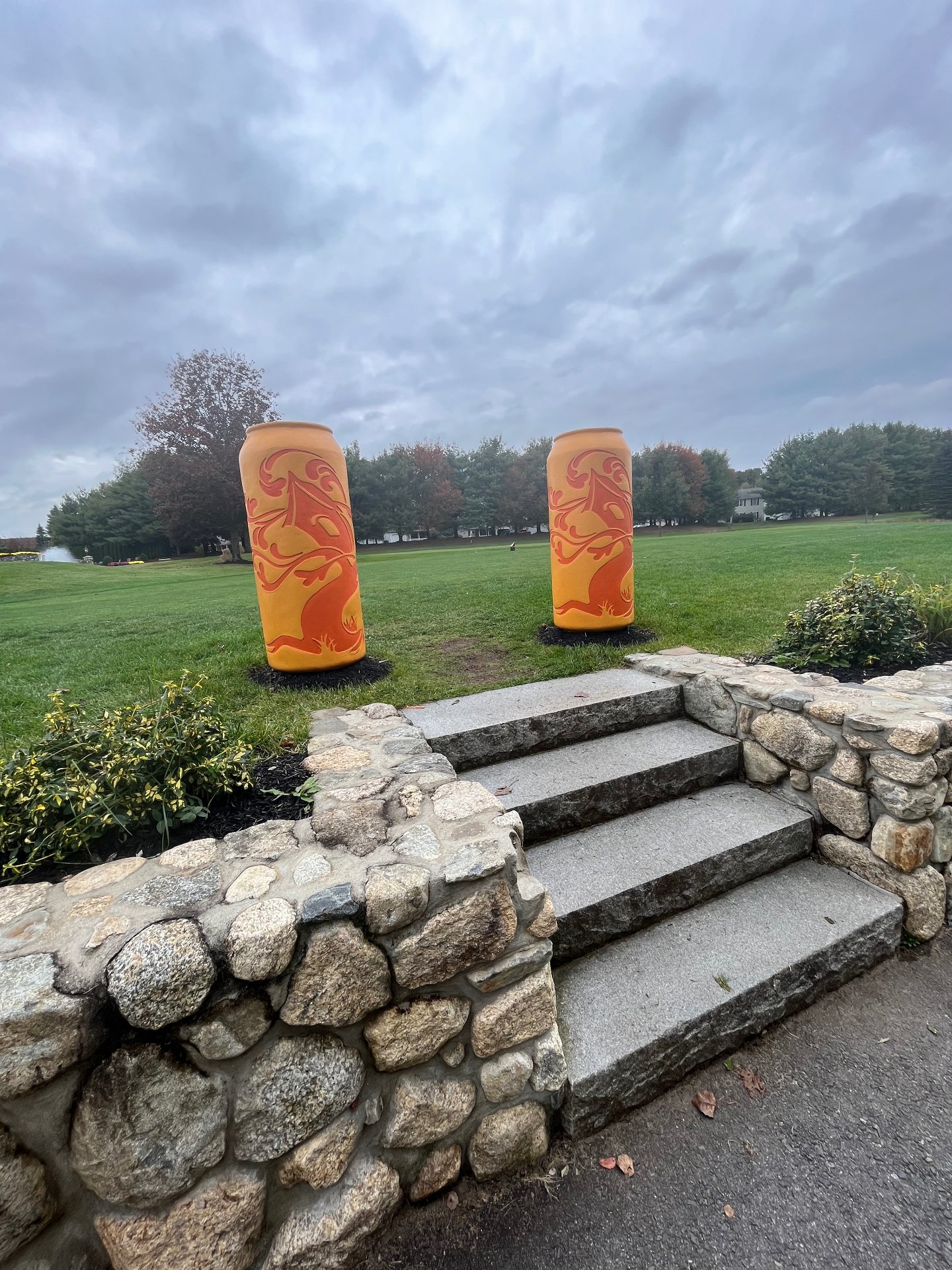 Granite steps and stone wall leading to the fairway at The Course at Tree House in Tewksbury, Massachusetts, with two oversized beer-can sculptures