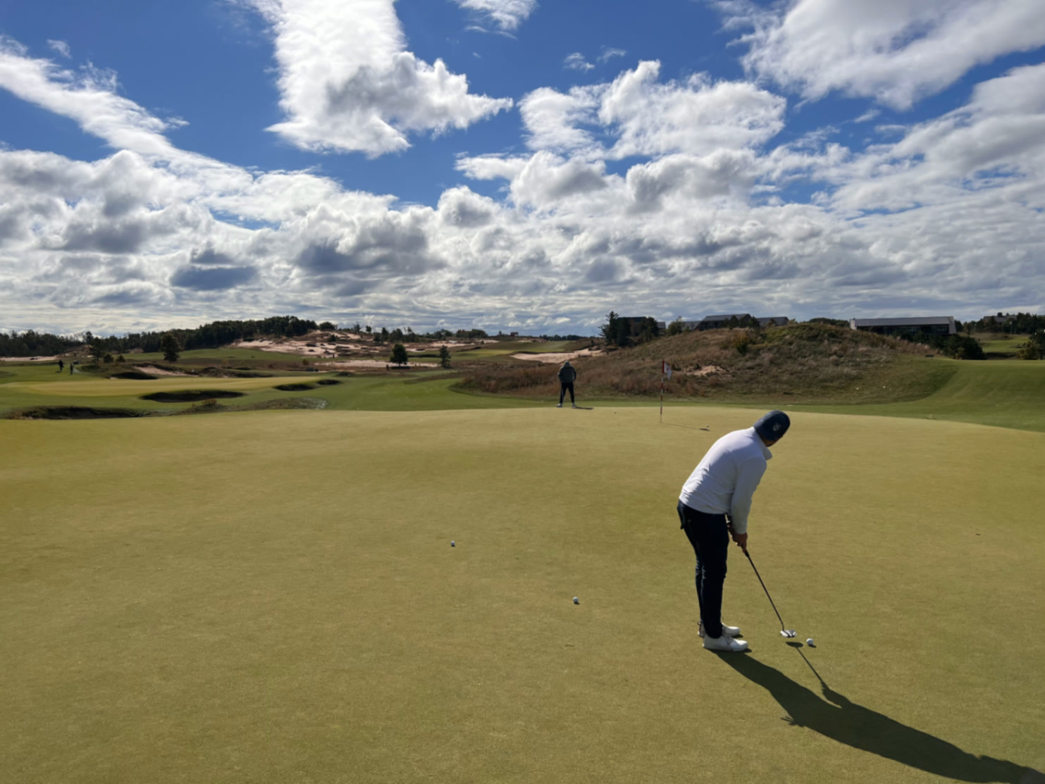 Golfer putting on a wide green at The Sandbox at Sand Valley under a big cloudy Wisconsin sky